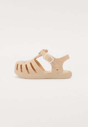 Beige småbørns-sandal med justerbar spænde-rem og ventileret overdel med en lille hvid sommerfugledekoration på tåområdet.