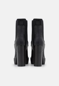 Bottines en cuir noir avec un talon haut et épais et des panneaux latéraux élastiques. Texture lisse et design minimaliste, avec des surpiqûres contrastantes.
