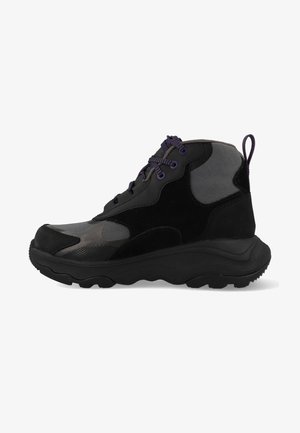 Sneaker mi-haut noir avec un mélange de matériaux lisses et texturés, des lacets violets et une semelle rembourrée pour le confort.
