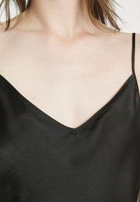 Svart satinkamisol med V-ringning och tunna band, som visar upp en mjuk textur och minimalistisk design.