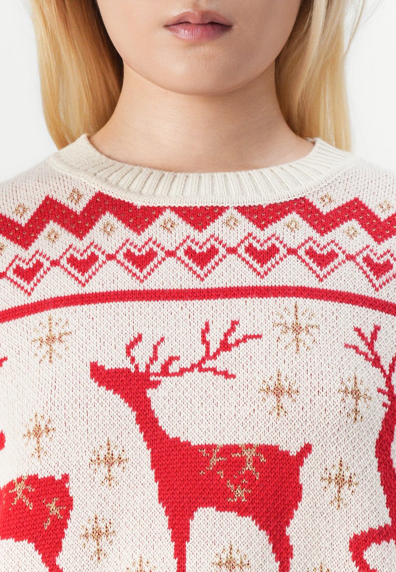 Jersey de punto en color crema con renos rojos y detalles dorados. Presenta un yugular decorado con corazones y copos de nieve. Cuello acanalado.