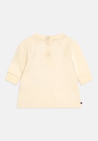 Haut à manches longues de texture crème avec un col rond, des boutons au dos et des poignets côtelés. Présente un motif à rayures horizontales.