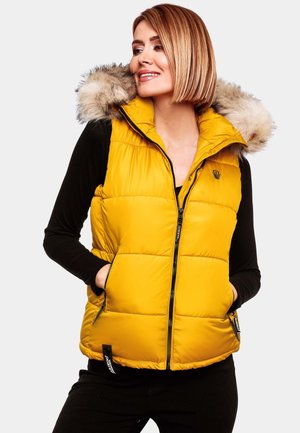 Gilet imbottito giallo con cappuccio bordato di pelliccia, con chiusura a zip e tasche laterali, abbinato a una maglietta nera a maniche lunghe.