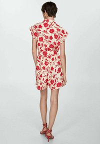 Florale romper in crème met een rood bloemenpatroon, korte mouwen, een getailleerde taille en een losse pasvorm, gecombineerd met rode strappy hakken.