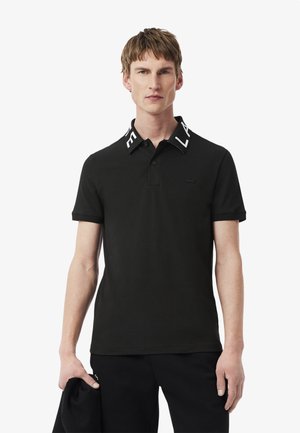 Polo nero con un logo bianco a contrasto sul colletto. Realizzato in tessuto morbido, ha maniche corte e una forma aderente.