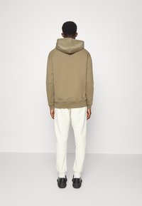 Sweatshirt caqui com capuz ajustável e punhos canelados, combinado com calças brancas e sapatos pretos. Design simples, material em mistura de algodão.