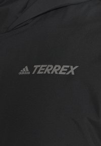 Musta kangas, jossa on heijastava Adidas-logo ja TERREX-br ändinimi painettuna pinnalle.