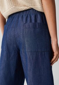 Dark blue denim pants with an elastic waistband, featuring two back pockets and a loose fit. The fabric has a smooth texture.