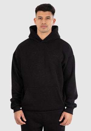 Zwarte hoodie met een voorzak, ribgebreide manchetten en zoom. Bevat een subtiel logo op de borst. Gemaakt van zachte, gestructureerde stof.