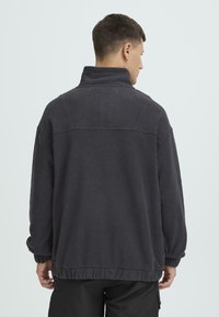 Tumehall fliisist pusak suure krae, langetatud õlgade ja elastseäärega. Omadusteks on pehme tekstuur ja lihtne disain.