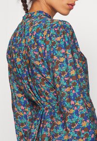 Floral dress featuring a blue base with multicolored flowers in pink, green, and brown. Puff sleeves and a high neckline with subtle gathering.