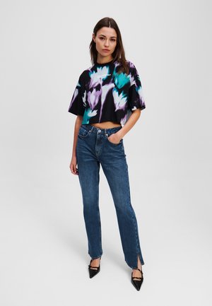 Cropped black t-shirt with turquoise and purple floral print, paired with straight blue jeans featuring a front slit and black pointed heels.