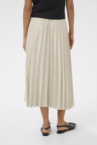 Gonna midi plissettata color crema con texture liscia, che cade sotto il ginocchio, abbinata a sandali piatti neri. La vista posteriore enfatizza le pieghe e il movimento.