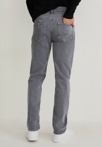 Jeans de mezclilla gris con un ajuste tapered, que cuentan con dos bolsillos traseros con costuras decorativas, y se llevan con zapatillas blancas.