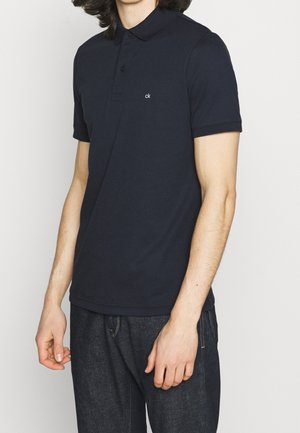 Granatowa koszulka polo z bawełny z kołnierzykiem i krótkimi rękawami, z małym białym logo po lewej stronie klatki piersiowej i prostym dołem.
