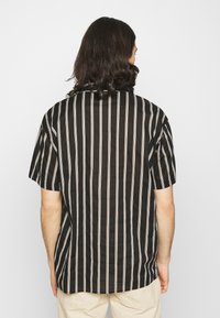 Camicetta nera a maniche corte con righe verticali bianche e beige; fit morbido e colletto semplice; tessuto dalla texture liscia, design rilassato sul retro.