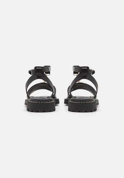 Černé sandály se šněrováním, s pevným podešví, nastavitelným kotníkovým páskem a minimalistickým designem. Mají texturovanou stélku a pevný úchop.