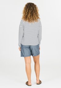 Mouwloze gestreepte shirt in zwart en wit, gecombineerd met denim shorts. Casual stijl met een relaxte pasvorm en opgerolde zoom, tegen een effen achtergrond.