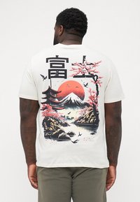 Crème kleurige t-shirt met korte mouwen featuring een kleurrijke Aziatische landschapsgrafiek, inclusief kersenbloesems, bergen en een pagode.