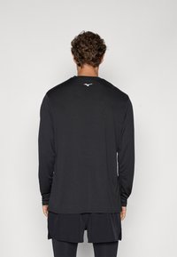 Svart langermet athletic skjorte med rund hals, laget av glatt stoff. Har en hvit logo på øvre rygg og en avslappet passform.