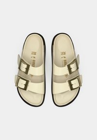 Πέδιλα στην απόχρωση της κρέμας με δύο ρυθμιζόμενα λουράκια, που διαθέτουν μεταλλικές αγκράφες. Έχουν ανατομικό εσωτερικό πέλμα και μαύρη εξωτερική σόλα. Μέγεθος 38.