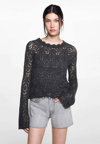 Dunkelgrauer, langärmeliger Häkelpullover mit gewelltem Ausschnitt, strukturiertem offenen Gewebe und lockerer Passform, kombiniert mit ausgebeulten grauen Shorts.
