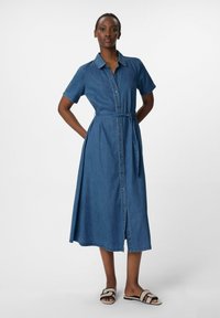 Sukienka koszulowa z dżinsu z krótkim rękawem, guziki z przodu, pasek w talii oraz rozcięcie po boku, w średnim odcieniu niebieskiego. Płaskie sandały z geometrycznym wzorem.