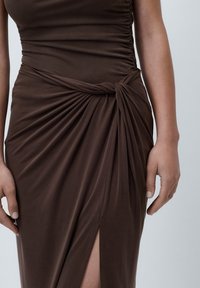 Brun drapert kjole med vridd midje, laget av glatt stoff, med en sidesliss og gatherdetaljer langs bodice.