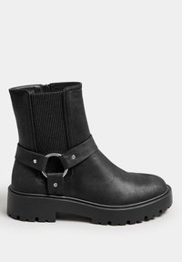 Black ankle boot with elastic side panels, smooth faux leather, round silver ring accent, and rugged treaded sole. Zipper closure on side.