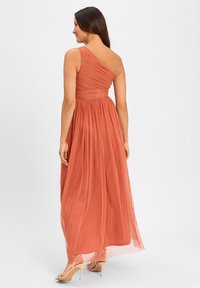Jedno-ramienna, rdzawa maxi sukienka z marszczonym dekoltem, zwiewnym dołem i teksturowanym materiałem. Połączona z cielistymi sandałami na wysokim obcasie.