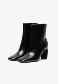 Black leather ankle boots with a square toe, zipper closure, and a block heel. Smooth texture with clean lines and minimalistic design.