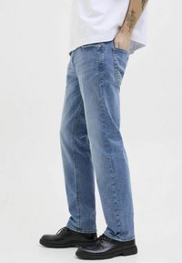 Jeans de mezclilla azul claro con corte recto, cinco bolsillos y detalles de costura sutiles, combinados con zapatos negros de cordones.