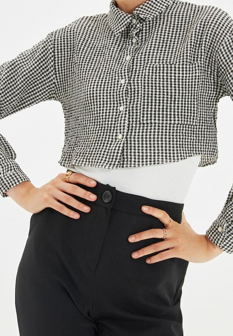Chemise boutonnée à manches longues à carreaux noirs et blancs, associée à un pantalon noir taille haute et un haut blanc en dessous.