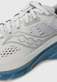 Light gray running shoe made of breathable mesh with a blue tinted sole, featuring decorative wave-like accents and reinforced eyelets for laces.