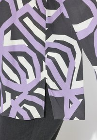 Bluse mit Kragen, die ein geometrisches Muster in Schwarz, Weiß und Lavendel zeigt. Leichter Stoff mit leicht strukturiertem Finish und seitlichen Schlitzen.