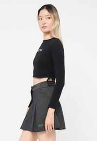 Crni dugi rukav uski top s bočnim nabranjem, kombiniran s plisiranom tamnosivom suknjom koja ima elastičnu pasicu i suptilne detalje.