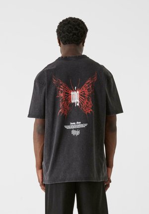 Black oversized t-shirt featuring a red butterfly graphic and white text on the back. Made of soft cotton with a textured finish.