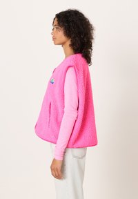 Roza jopiči iz flisa z teksturno površino, odprtim dizajnom, dvema stranskima žepoma in majhno logotipno značko spredaj.