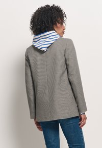 Blazer a motivo pied de poule grigio, con cappuccio a righe blu e bianche. La vestibilità è aderente, con maniche lunghe e orlo dritto.