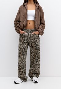 Brown zip-up jacket, white cropped tank top, and loose-fitting leopard print sweatpants. Footwear is silver athletic shoes.