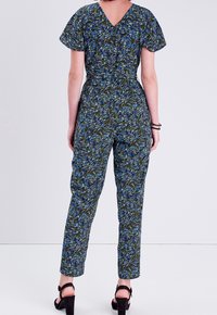 Combinaison à motifs floraux avec un décolleté en V, des manches courtes, une taille cintrée et des jambes fuselées dans les couleurs bleu, vert et noir.