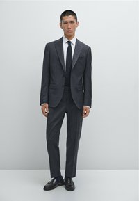 Dark gray suit with a notched lapel, white shirt, black tie, and black shoes. Fitted design with smooth texture and minimal accents.