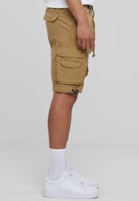 Khaki cargoshorts met meerdere zakken, verstelbare taille met trekkoord en duurzaam materiaal. Gecombineerd met witte sneakers en crew-sokken.