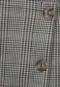 Grijs en zwart houndstooth stof met een gladde textuur, voorzien van een grote, ronde knoop in een neutrale tint. Close-up van het textielpatroon.
