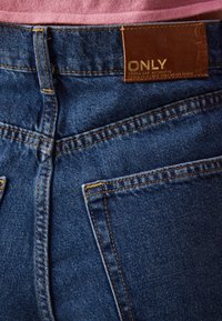 Blue denim jeans with orange stitching, featuring a leather label marked "ONLY" at the back waistband and two back pockets.