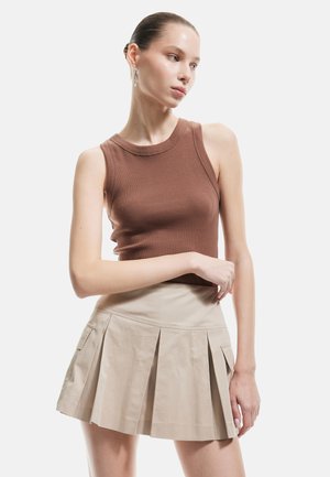 Top in cotone marrone a costine abbinato a una mini gonna plissettata beige con tasche laterali. L'outfit mette in evidenza una silhouette aderente.