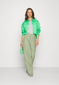 Casaco bomber de cetim verde, blusa cinza, calças largas em padrão houndstooth verde, bolsa verde combinando e sapatos de salto aberto verdes. Texturas suaves.