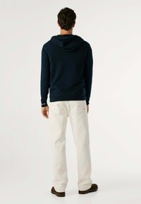 Mornarska kapuca z vrvico, v kombinaciji s kremnimi džinsom. Obleka se ponaša s preprostim dizajnom in tesnim prileganjem.