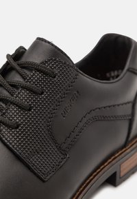 Zapatos de cuero negro con un revestimiento texturizado, cordones redondos y un acento de tacón de madera. Logo de la marca en relieve en el lateral.