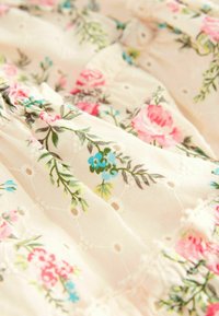 Cream fabric with pink and blue floral print and eyelet embroidery detail, showing gathered and ruched texture.